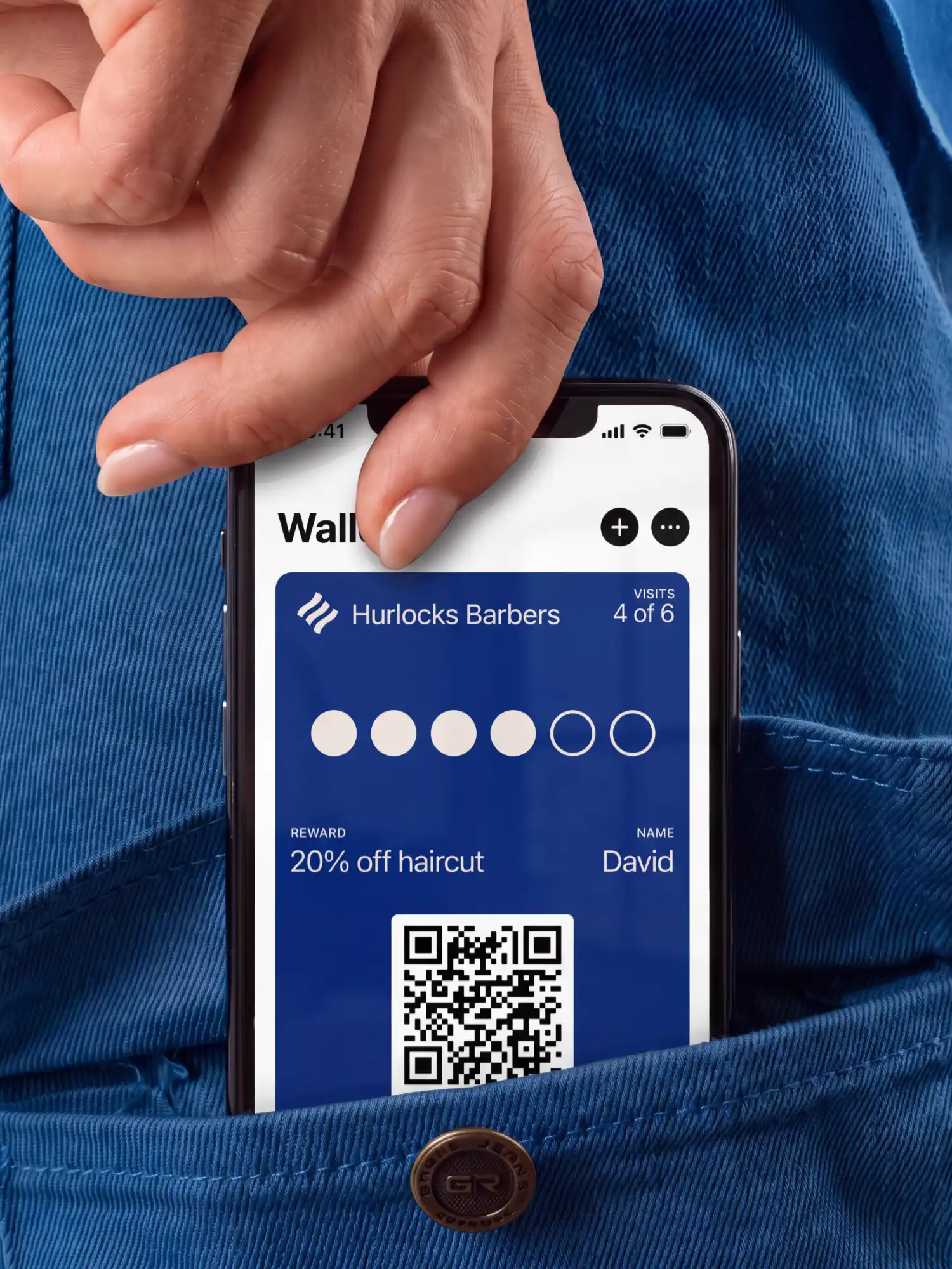 A phone showing a Hurlocks Barbers visits card in Apple Wallet, 4 of 6 visits, being slipped into a jeans pocket